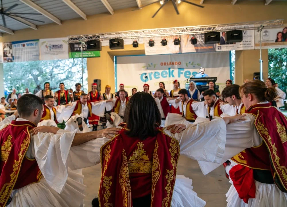 Greek dancers in traditional costumes dancing in a linked circle at Orlando Greek Fest